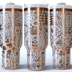 May include: Three tall insulated tumblers with handles, featuring a white base and a metallic copper pumpkin and floral pattern. Each tumbler has a white lid and a tapered base, displaying a repeating design of pumpkins, leaves, and vines.