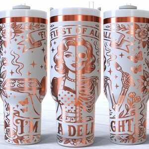 May include: White insulated tumbler with a rose gold design. The design features a woman's face, half human and half skeleton, with the text "FIRST OF ALL I'M A DELIGHT". Includes a handle and a lid.