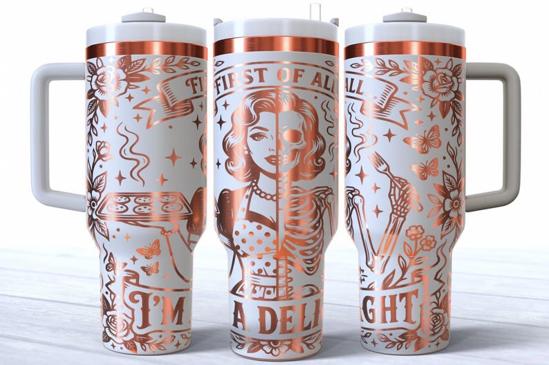 May include: White insulated tumbler with a rose gold design. The design features a woman's face, half human and half skeleton, with the text "FIRST OF ALL I'M A DELIGHT". Includes a handle and a lid.