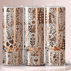 May include: Three cylindrical tumblers with clear lids and straws, featuring a white background and a metallic copper-colored pattern of pumpkins, leaves, flowers, hearts, and checkered designs covering the entire exterior surface of each cup.