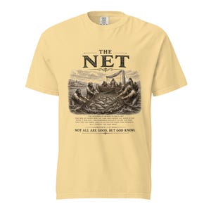 May include: A pale yellow short-sleeve t-shirt featuring a black graphic of fishermen pulling a net from a lake. The text reads THE NET, a passage from Matthew 13:47-48, and the phrase NOT ALL ARE GOOD, BUT GOD KNOWS in black lettering.