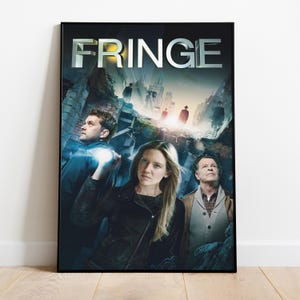 May include: A framed poster with the word "FRINGE" in silver lettering. The poster shows three people in the foreground with a cityscape and silhouetted figures in the background. The poster is in a black frame.