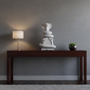 Könnte beinhalten: Ein dunkelbrauner Konsolentisch mit einer weißen Kobraskulptur, einer kleinen Topfpflanze und einer Lampe mit beigem Lampenschirm. Der Tisch steht vor einer grauen Wand, mit einem grauen Teppich auf dem Boden.