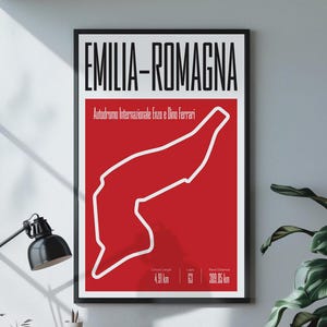 Op de afbeelding: Een ingelijste poster met de lay-out van het Emilia-Romagna circuit in wit tegen een rode achtergrond. De poster bevat de tekst "EMILIA-ROMAGNA" en circuitdetails. De poster hangt aan een witte muur bij een raam.