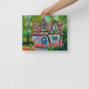 May include: A colorful painting of a whimsical cottage with a brown roof, blue door, and green accents. The cottage is surrounded by vibrant pink and red flowers, with a lush green forest in the background. The artwork is held by a person.