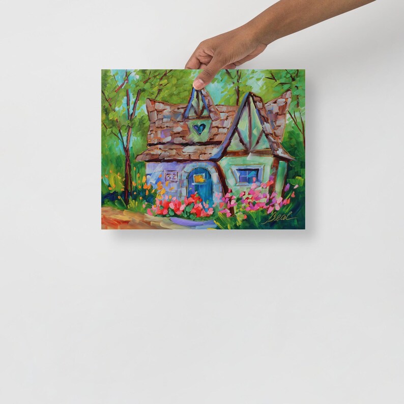 May include: A colorful painting of a whimsical cottage with a brown roof, blue door, and heart-shaped detail. The cottage is surrounded by vibrant flowers and lush greenery, creating a charming, fairytale-like scene. The artwork is held by a person.