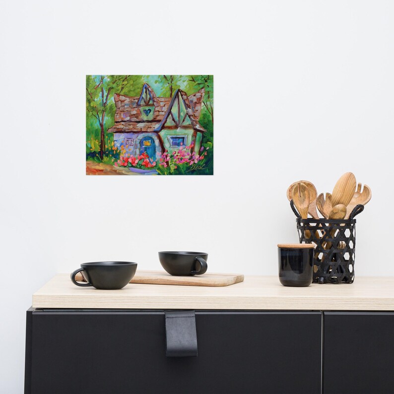 May include: A colorful painting of a whimsical cottage with a blue door and a heart-shaped detail on the roof. The cottage is surrounded by flowers and trees, with a vibrant, impressionistic style. The artwork is displayed on a white wall.