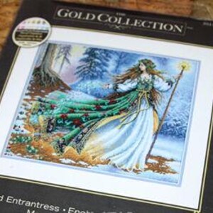 Puede incluir: Un kit de punto de cruz Dimensions Gold Collection con la ilustración de una figura de pelo largo con un vestido blanco y verde, sosteniendo un bastón brillante en un bosque nevado. El texto dice The Gold Collection y Entrantress.