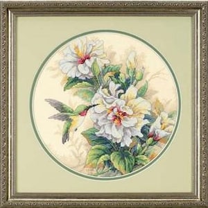 Könnte beinhalten: Ein gerahmtes Kreuzstichbild mit einem grünen und roten Kolibri, der neben weißen und gelben Hibiskusblüten mit grünen Blättern schwebt, vor einem cremefarbenen Hintergrund in einem kreisförmigen Rahmen und einem strukturierten silbernen Metallrahmen.