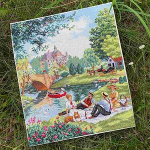 May include: A rectangular cross-stitch embroidery depicting a pastoral scene with a stone bridge, a large house, a horse-drawn carriage, and a group of people having a picnic by a river. The scene includes a red boat, swans, and a dog.