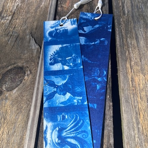 May include: Two blue cyanotype bookmarks with white tassels. The bookmarks feature a series of images including a monster, a rabbit, and an octopus.