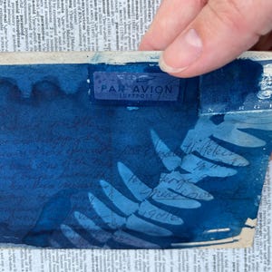 May include: A blue envelope with a "PAR AVION LUFTPOST" stamp. The envelope features a fern leaf design and handwritten text in blue ink. The text reads "Norsk Ti-Felis 18.7.1946 To Grandma 1946".
