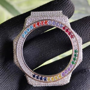 Puede incluir: Un bisel de reloj plateado con un arcoíris de piedras preciosas que rodea la esfera. El bisel está incrustado con pequeñas piedras transparentes. Las piedras preciosas están dispuestas en un patrón circular de rojo, naranja, amarillo, verde, azul y morado.