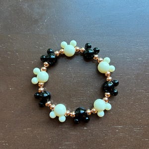 Puede incluir: Una pulsera de cuentas con dijes de cabeza de Mickey Mouse negros y crema alternados. La pulsera est&aacute; ensartada en un cord&oacute;n el&aacute;stico de color cobre, creando un accesorio l&uacute;dico y caprichoso.