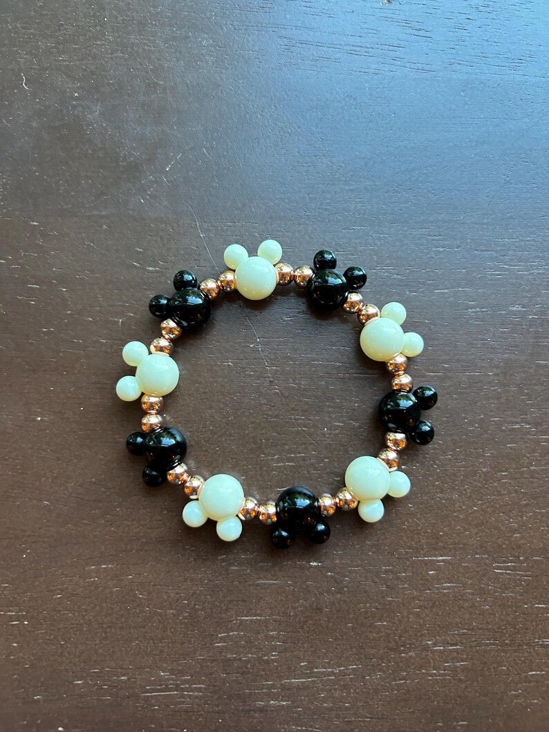 Puede incluir: Una pulsera de cuentas con dijes de cabeza de Mickey Mouse negros y crema alternados. La pulsera est&aacute; ensartada en un cord&oacute;n el&aacute;stico de color cobre, creando un accesorio l&uacute;dico y caprichoso.