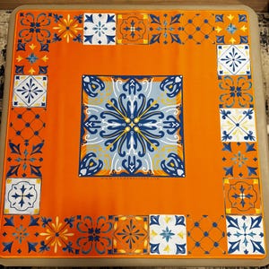 K&ouml;nnte beinhalten: Quadratischer, orangefarbener Mahjong-Tisch mit dekorativem Fliesendesign. Die Mitte zeigt ein gro&szlig;es blau-wei&szlig;es Blumenmuster, und der Rand hat kleinere Fliesenmotive in Blau, Wei&szlig; und Orange. Die Website www.ladiesmahjong.com ist sichtbar.