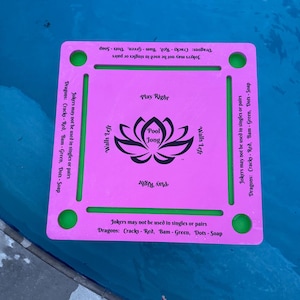 May include: A pink rectangular Pool Jong game board with green accents and text. The board features the words "Pool Jong" with a lotus flower design. The text "Play Right" and "Walls Left" are also visible. The board is floating in water.