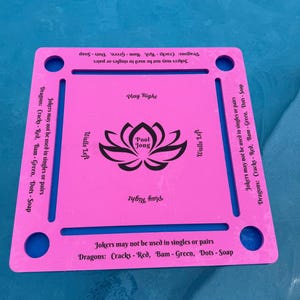 May include: A pink and blue Pool Jong board with a lotus flower logo in the center. The board has text that reads "Play Right" and "Walls Left". The text "Jokers may not be used in singles or pairs" is also visible.