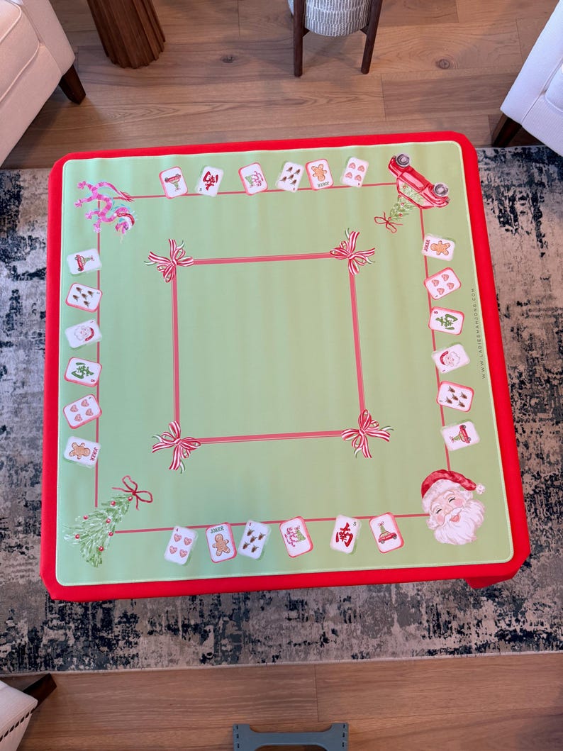 May include: A square, Christmas-themed game table cover with a light green centre and a red border. The cover features a red square border, red bows, and Christmas-themed card illustrations. A Santa Claus illustration is in the corner.