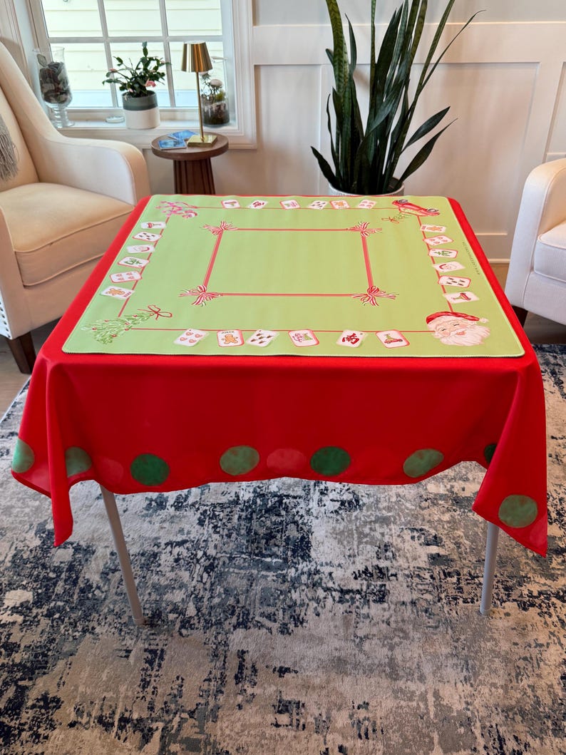 May include: A festive Christmas tablecloth. The base is red, with a light green central panel. The green panel has a red border and decorative elements. The red border has green polka dots. Santa Claus and other festive images are printed on the tablecloth.
