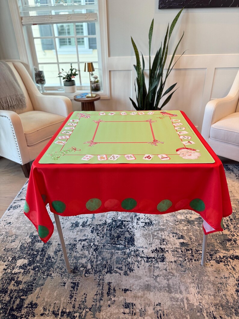 May include: A Christmas-themed tablecloth. The top is light green with red and white decorative elements, including Santa Claus and gift boxes. The tablecloth's border is red with large green polka dots. The table is supported by silver legs.
