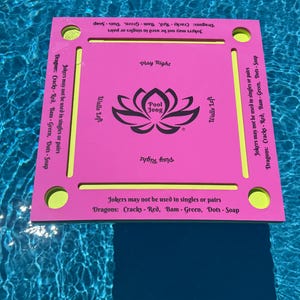 May include: A square pink floating game board with a central black lotus graphic labeled Pool Jong. The board features yellow accents, four corner circular cutouts, and text stating Jokers may not be used in singles or pairs and Dragons: Cracks - Red, Bam - Green, Dots - Soap.