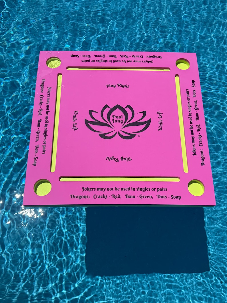 May include: A square pink floating game board with a central black lotus graphic labeled Pool Jong. The board features yellow accents, four corner circular cutouts, and text stating Jokers may not be used in singles or pairs and Dragons: Cracks - Red, Bam - Green, Dots - Soap.