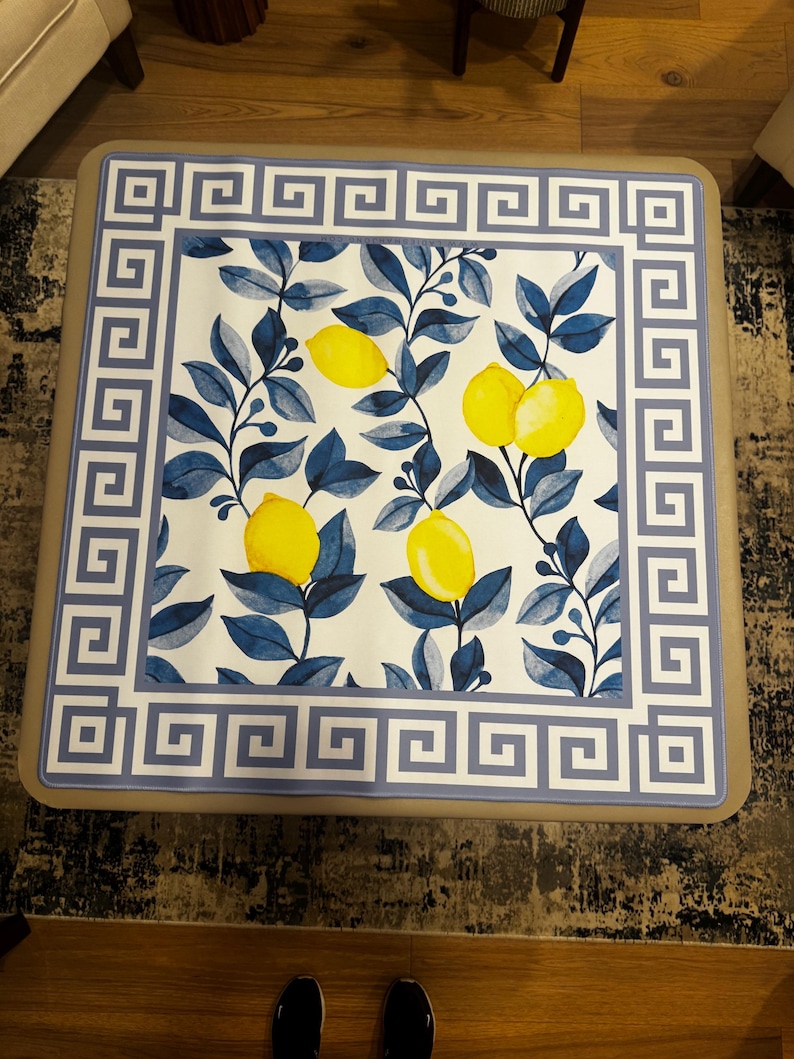 Puede incluir: Mesa de centro cuadrada con una tapa decorativa con un dise&ntilde;o de lim&oacute;n y hojas. El dise&ntilde;o incluye limones amarillos, hojas azules y un fondo blanco. El borde tiene un patr&oacute;n de clave griega azul y blanco.