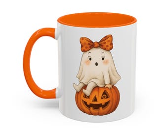 May include: White ceramic mug with an orange interior and handle. The mug features a cartoon ghost with a bow sitting on a carved pumpkin. The ghost and pumpkin are in the center of the mug, perfect for Halloween.
