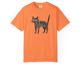May include: Orange t-shirt featuring a black and white illustration of a cat. The cat is drawn with vertical lines, giving it a textured appearance. The cat has large, round eyes and a long tail. The shirt is made of a soft material.