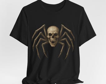 May include: Black t-shirt featuring a detailed illustration of a skull-spider hybrid. The skull has visible teeth and is the focal point, with spider legs extending outwards. The design is in shades of brown and beige.