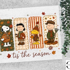 May include: A rectangular graphic print featuring Snoopy, Lucy, Woodstock, and Charlie Brown dressed in autumn attire within four vertical panels. The characters are surrounded by fall leaves and pumpkins, with the text 'tis the season' below.