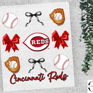 May include: A design featuring baseballs, mitts, red bows, and the Cincinnati Reds logo. The words "Cincinnati Reds" are written in a script font. The design includes black bows and a white background.