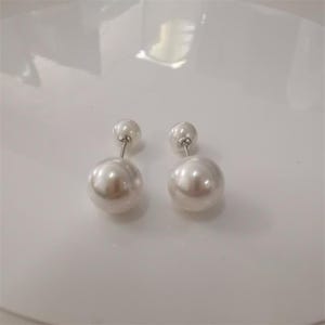 May include: A pair of pearl earrings. Each earring has a large, round, lustrous pearl below a smaller pearl. The earrings have a silver-coloured post. The pearls have a soft, white sheen.