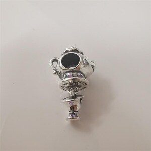 Può includere: Un charm in argento sterling a forma di teiera con una tazzina da tè pendente. La teiera presenta un'apertura circolare, incisa con il testo Pandora e S925, e include piccoli accenti in smalto viola sulla base e sulla tazzina da tè.