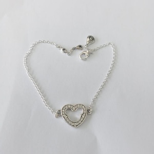 Peut inclure: Un bracelet en argent avec un charm en forme de c&oelig;ur int&eacute;grant une silhouette de Mickey Mouse. Le charm est serti de petits pierres pr&eacute;cieuses transparentes. Le bracelet a une cha&icirc;ne fine et une fermeture &agrave; mousqueton.