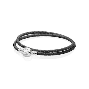May include: A double-wrap bracelet featuring a black braided leather cord and a polished silver-tone spherical clasp. The clasp is engraved with the text PANDORA and has a ribbed cylindrical connector on each side of the sphere.