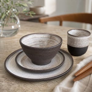 May include: A ceramic dinnerware set consisting of a large plate, a smaller plate, a bowl, and a cup. Each piece features a dark brown base with a speckled white glaze on the interior and upper surfaces, creating a two-tone appearance.