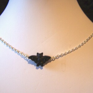Può includere: Una collana a catena d'argento con un ciondolo a forma di pipistrello nero.