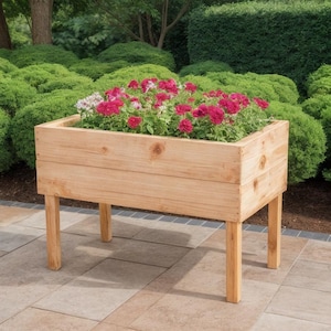May include: A wooden planter box, filled with pink and white flowers, stands on four legs. The light-coloured wood planter is set on a stone patio, with green bushes in the background. The planter measures approximately 76 cm in length.