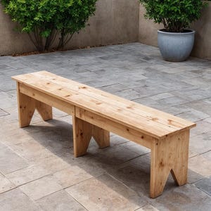 Può includere: Una panca in legno chiaro con seduta rettangolare e gambe angolate. La panca è realizzata con assi di legno ed è lunga circa 152 cm. È posizionata su un patio in pietra.