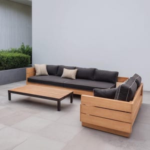May include: A modern outdoor furniture set comprising a wooden sofa, loveseat, and coffee table. The sofa and loveseat have dark grey cushions with white piping and scatter cushions. The coffee table has a dark metal frame and wooden top.