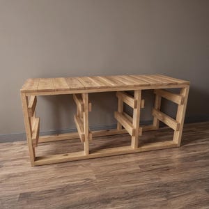 Pu&ograve; includere: Una consolle in legno chiaro con piano a doghe e base geometrica. Il tavolo &egrave; realizzato in legno naturale e ha una forma rettangolare. Il tavolo misura circa 152 cm di lunghezza, 41 cm di larghezza e 76 cm di altezza.