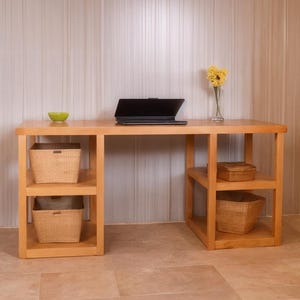 Peut inclure: Un bureau en bois clair avec deux étagères intégrées, chacune contenant un panier en osier. Un ordinateur portable est posé sur le bureau, et un petit vase avec des fleurs jaunes est également présent. Un petit bol vert est sur le bureau.