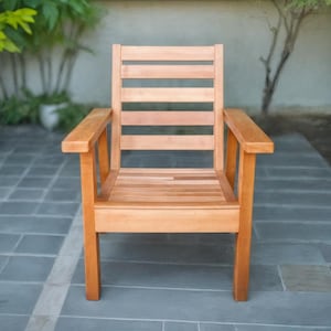 May include: A wooden outdoor chair with a natural finish. The chair has a slatted back and seat, with armrests. The chair is made of light brown wood and is placed on a grey tiled surface.