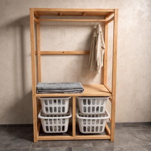 May include: A wooden open wardrobe with a hanging rod, shelf, and two levels of white plastic baskets. A folded gray blanket rests on the shelf. A beige jacket hangs from the rod.