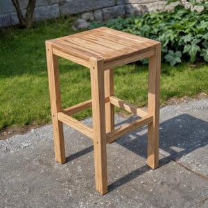Peut inclure: Un tabouret de bar en bois brun clair avec une assise carrée et quatre pieds. L'assise est constituée de lattes de bois horizontales. Le tabouret est à l'extérieur sur une surface en béton, avec de l'herbe et de la verdure en arrière-plan. Hauteur: environ 76 cm.
