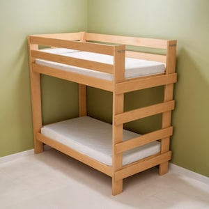 May include: A light-colored wooden bunk bed with two levels. Each level has a white mattress. The bed frame has a simple design with horizontal slats for safety. The bed is in a room with light green walls.
