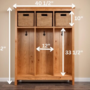 May include: A wooden entryway organizer with three sections. It features three woven baskets at the top, three coat hooks, and a lower shelf. The unit is 40.5 inches wide, 52 inches tall, and 12 inches deep. The baskets are 10 inches tall, and the open sections are 33.5 inches tall.