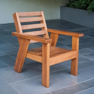 May include: A wooden armchair with a natural finish. The chair has a slatted back, armrests, and a seat made of wooden planks. The chair is constructed with visible joints and a sturdy frame, suitable for outdoor or indoor use.